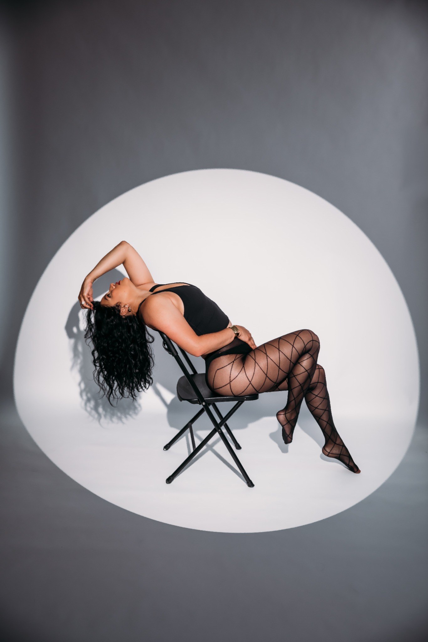 Shay reclining confidently on a chair during a studio chair dance photoshoot.