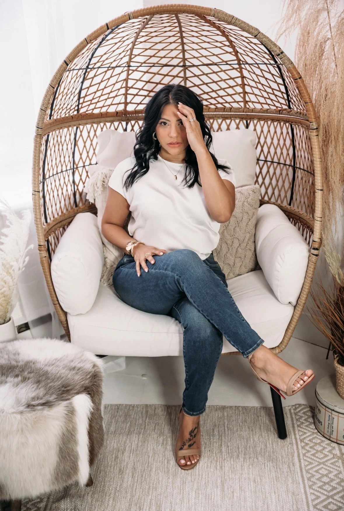 Shay wearing a white shirt and jeans, seated in a woven chair